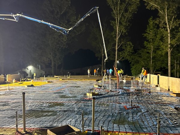 Rebar mat and yellow vapor barrier ready for a nighttime concrete slab pour under work lights