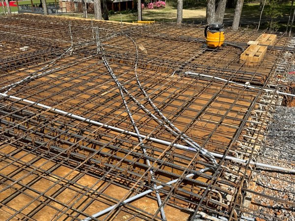 Rebar mesh and conduit runs placed ahead of a slab pour, with the Youth Villages campus visible in the background