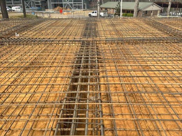 Rebar mesh and thickened footing trench for a slab pour, with the new metal building taking shape across the site