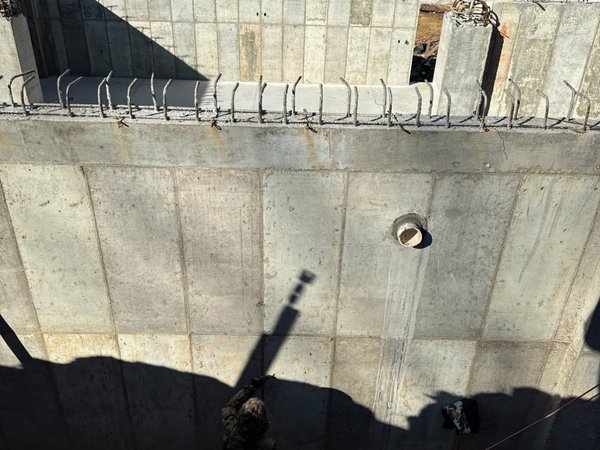 Formed and poured concrete foundation wall with exposed rebar dowels ready for the next lift, viewed from above
