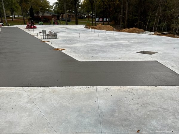 Finished broom-troweled concrete slab with a contrasting dark accent strip at a completed building pad