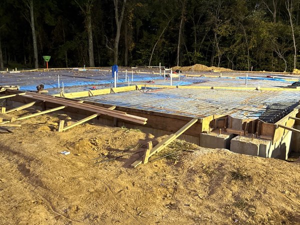 Vapor barrier and rebar mesh in place for a large slab-on-grade pour, with footing forms visible at the near corner