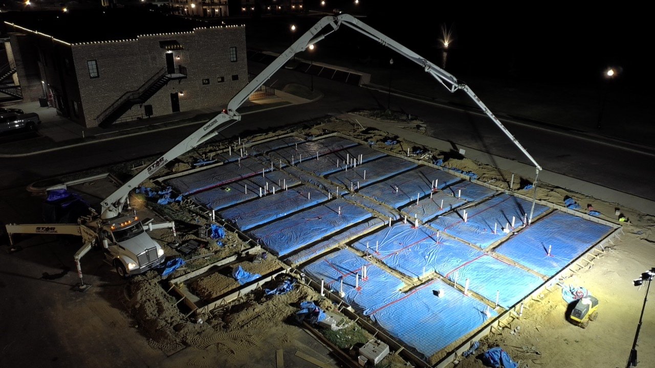 Night pour setup for a new ground-up commercial building — concrete pump truck positioned over a fully formed and reinforced foundation ready for placement